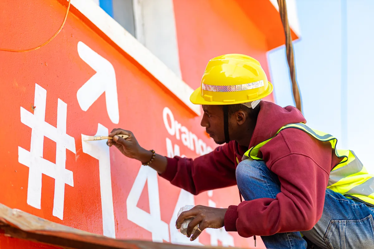 Peinture publicitaire en cours de réalisation sur un mur de marque Orange